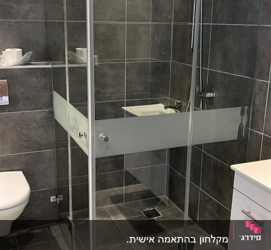 מקלחון זכוכית עם ראש מקלחת מתכתי על קיר אריחים אפור